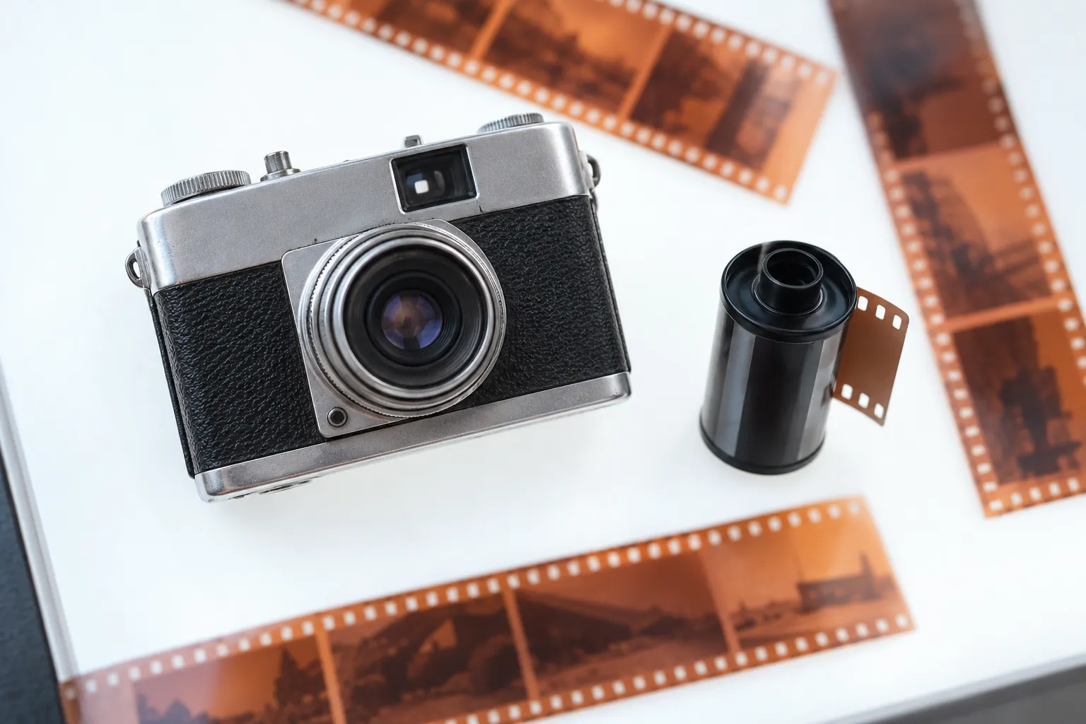 A small silver film camera and 35mm cassette with developed negative strips on a light table.